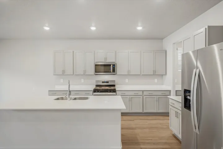 Modern kitchen featuring light gray cabinetry, white countertops, stainless steel appliances, and wood-finish flooring