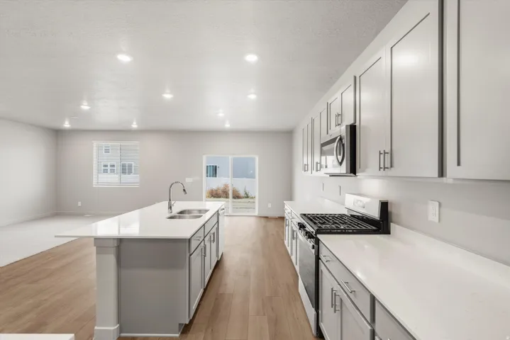 Modern kitchen featuring a large island with an undermount sink, light-colored cabinetry, stainless steel appliances, white countertops, and wood-finish flooring
