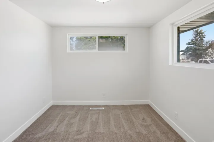 Neutral-toned carpeting enhances this bright room with multiple windows, clean white walls, and matching baseboards