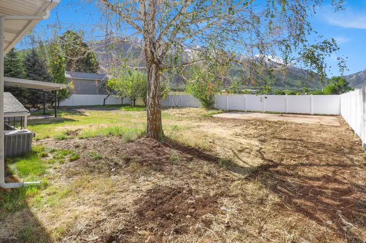 Expansive backyard featuring a mature tree, white privacy fencing, and a concrete pad
