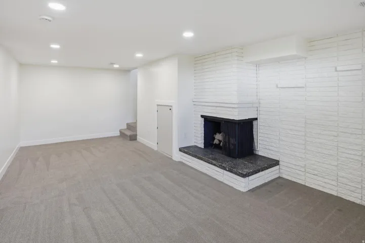 Spacious room featuring a white painted brick fireplace with a dark stone hearth