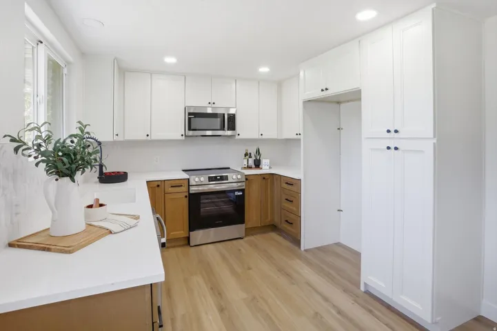 Modern kitchen featuring white shaker cabinetry, stainless steel appliances, light wood-finish flooring, white countertops, and a full-height tile backsplash