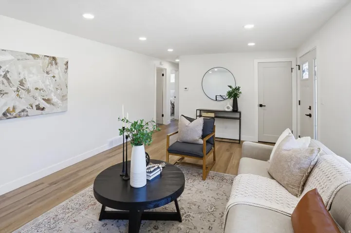 Bright living space featuring recessed lighting, wood-finish flooring, a modern front entry door with glass panels, a solid interior door with black hardware, and crisp white baseboards