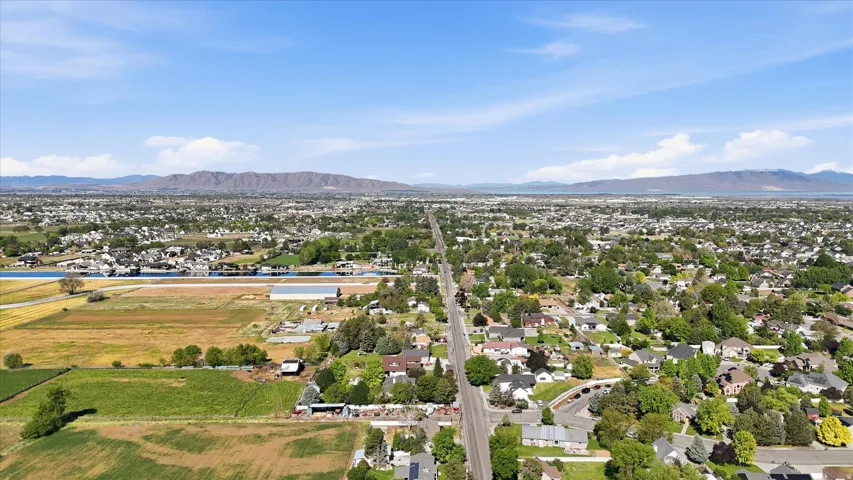 Expansive aerial perspective showcasing a residential area with mature trees, bordered by agricultural fields and a distinct body of water