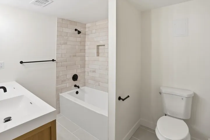 Bathroom featuring a white vanity with integrated sink, matte black fixtures, a white bathtub with subway tile surround, and light gray floor tiles