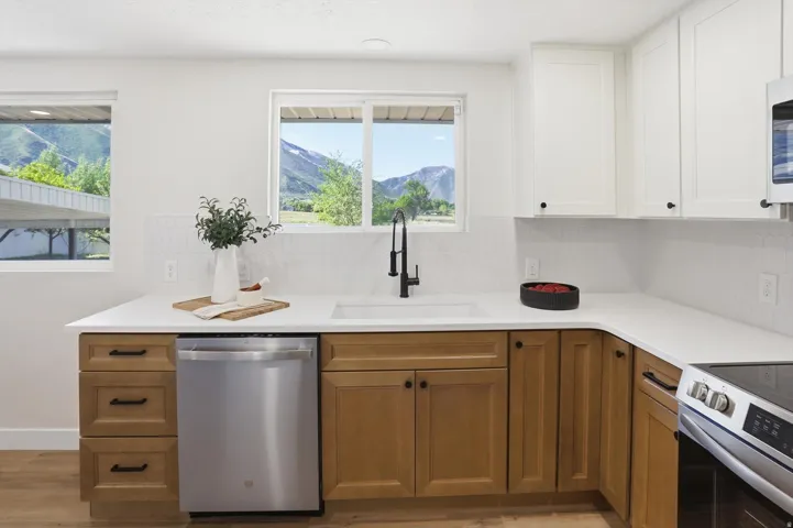 Modern kitchen featuring two-tone cabinetry, white countertops, a stainless steel dishwasher, and a deep single-basin sink with a matte black faucet