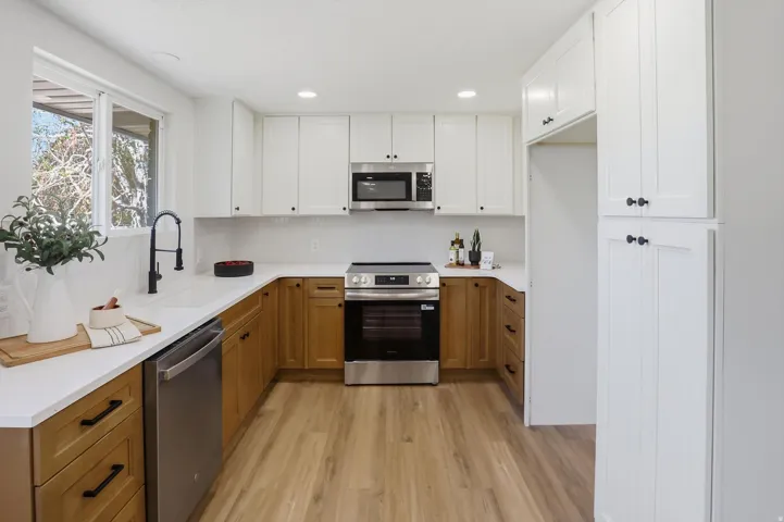 Kitchen featuring two-tone cabinetry with black hardware, stainless steel appliances, white countertops, and wood-finish flooring