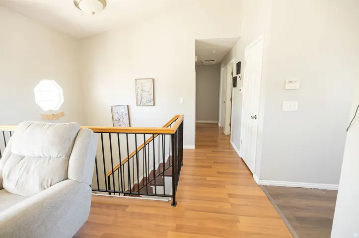 Upper level landing featuring wood-finish flooring, a contemporary black metal and wood staircase railing, and a hallway leading to interior doors