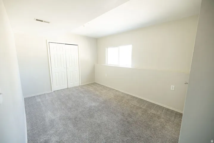 Spacious interior room featuring light gray carpeting, white painted walls, a white bi-fold closet door, a large window, and white baseboards
