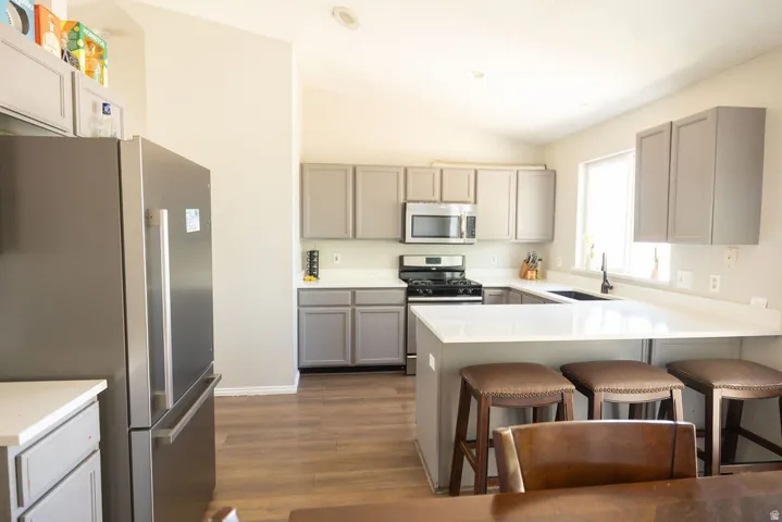 Kitchen featuring light gray cabinetry, white countertops, stainless steel appliances, wood-finish flooring, and a breakfast bar