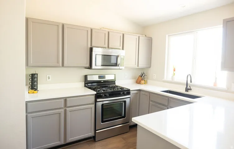Modern kitchen featuring light gray cabinetry, stainless steel appliances, white countertops, a gas range, and a black undermount sink with a gooseneck faucet
