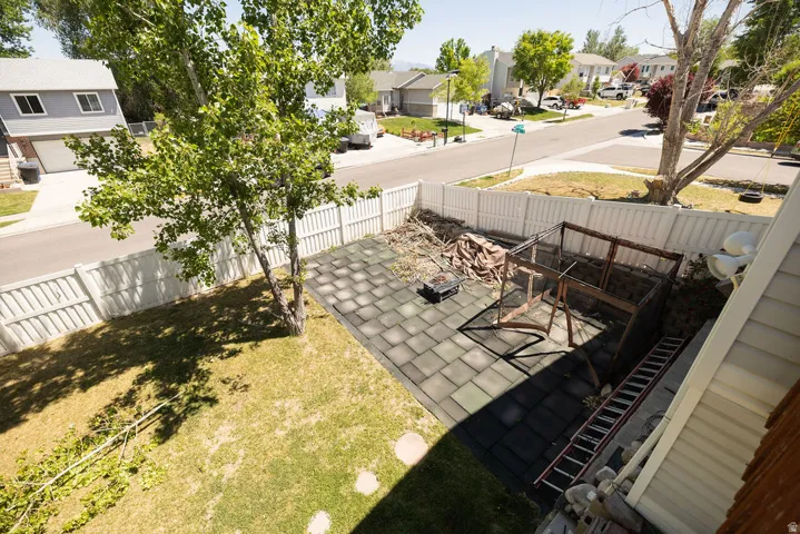 Fenced backyard featuring a paved patio area, green lawn, and mature trees