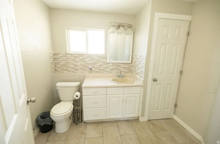 Bathroom featuring a white vanity with integrated sink, a rectangular mirror, and a window above a tiled backsplash