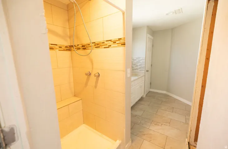 Shower stall featuring light-toned rectangular wall tiles, a decorative mosaic accent band, and a built-in bench