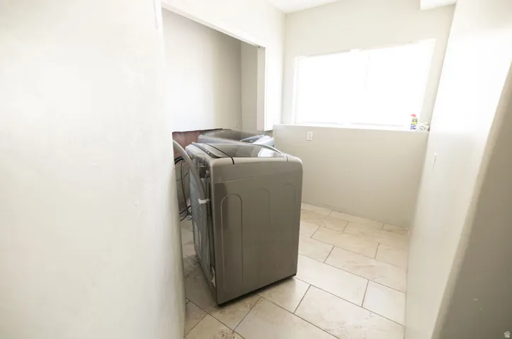 Utility room featuring light-toned tile flooring, neutral wall paint, and a window with horizontal blinds