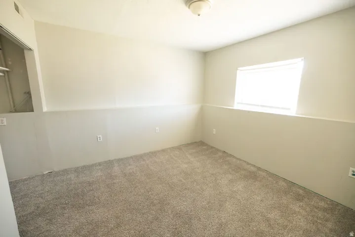 Carpeted room with light-toned walls and a window featuring blinds