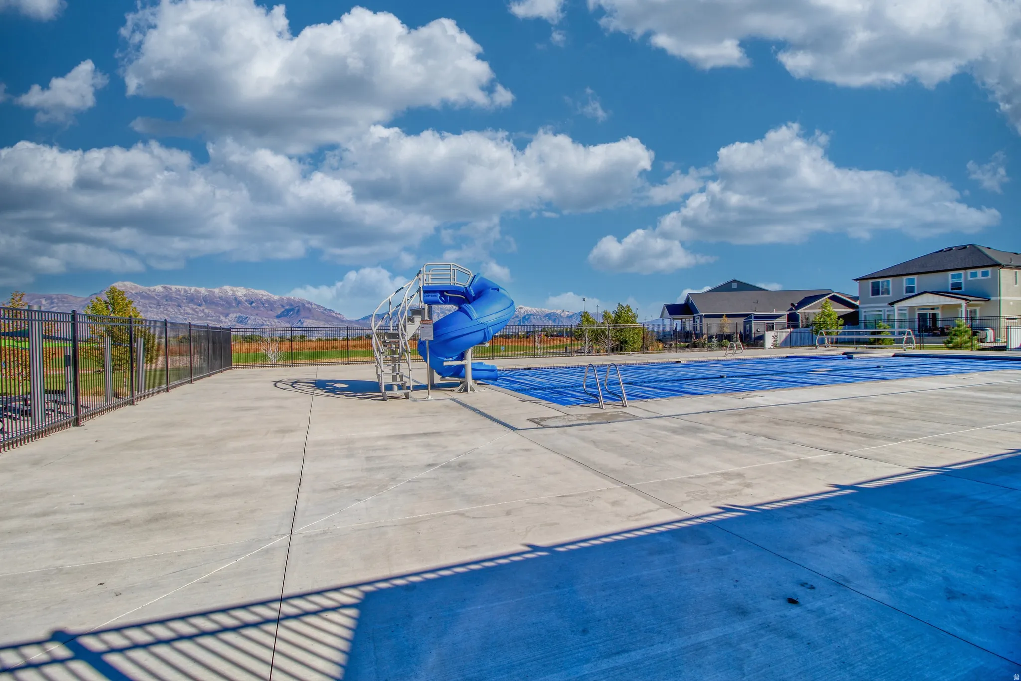 Outdoor swimming pool area featuring a prominent blue water slide, concrete decking, and a black perimeter fence
