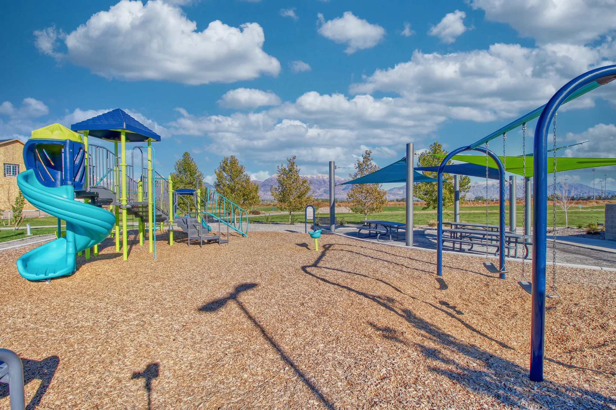 Community playground featuring a spiral slide, swing set, and shaded picnic tables on a wood-chip surface