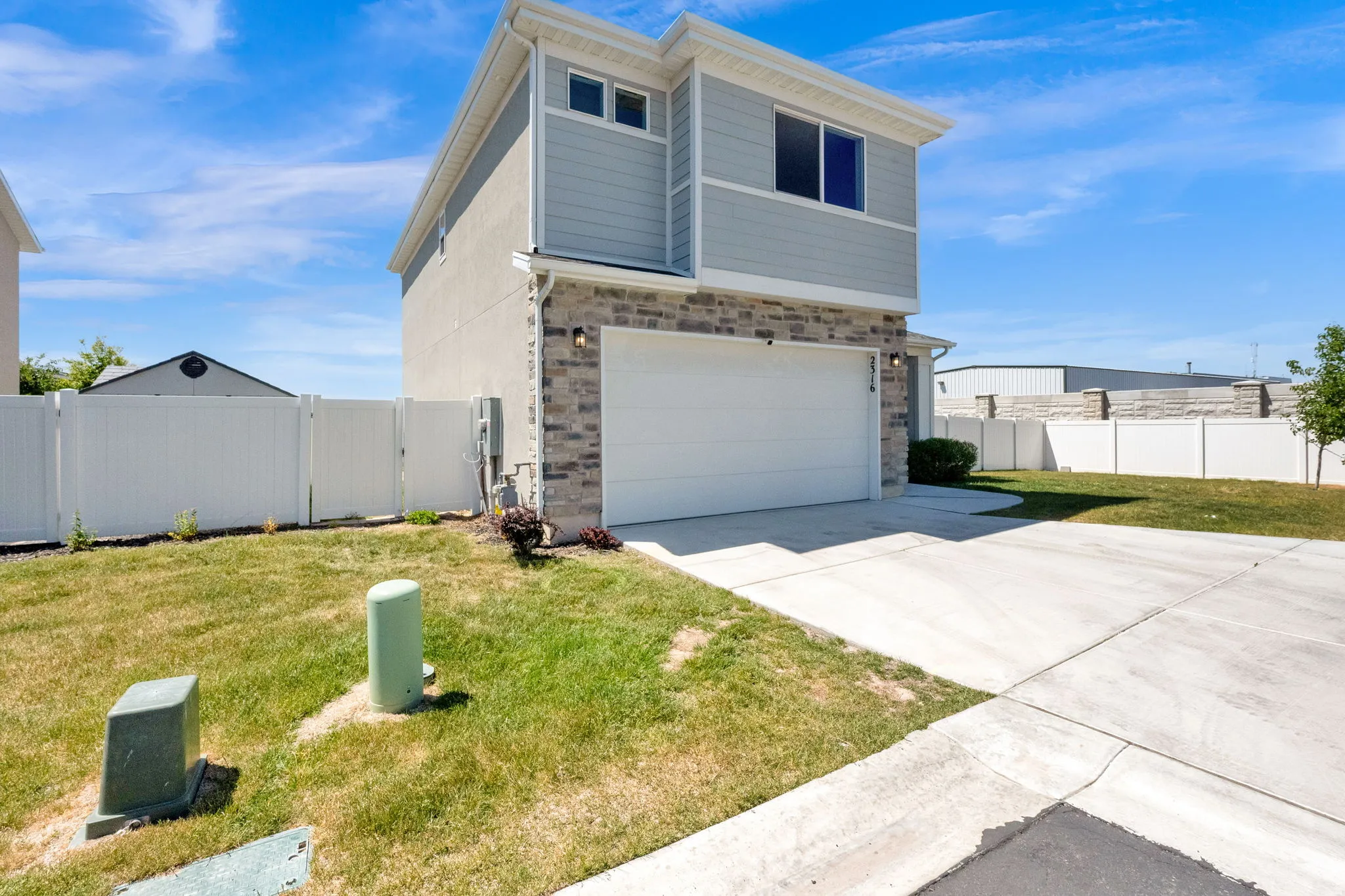 Contemporary home exterior featuring a light gray siding, stone veneer accents, an attached garage, a concrete driveway, and a white privacy fence