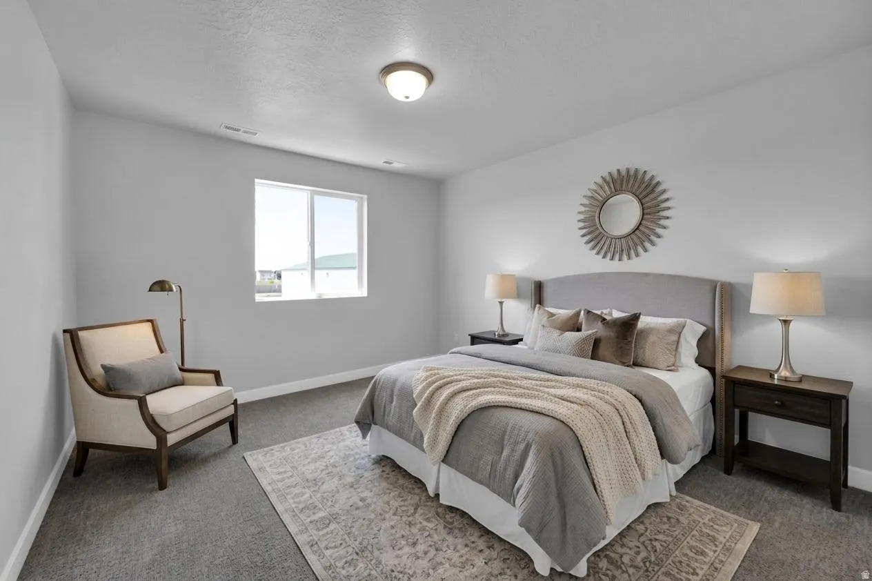 Spacious bedroom featuring neutral wall tones, soft gray carpeting, and a window for natural illumination