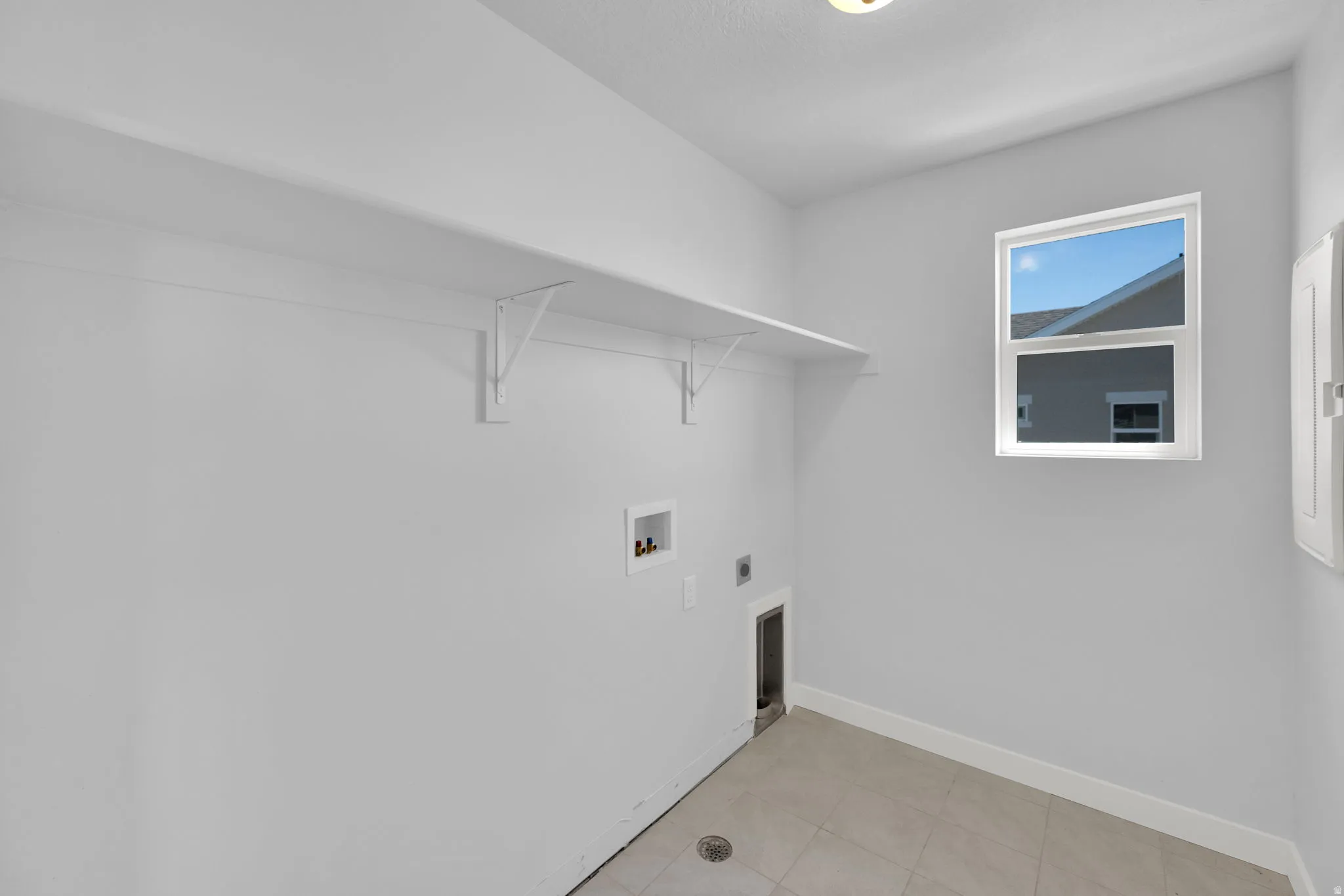 Utility room featuring a single window, overhead shelving, and tile flooring