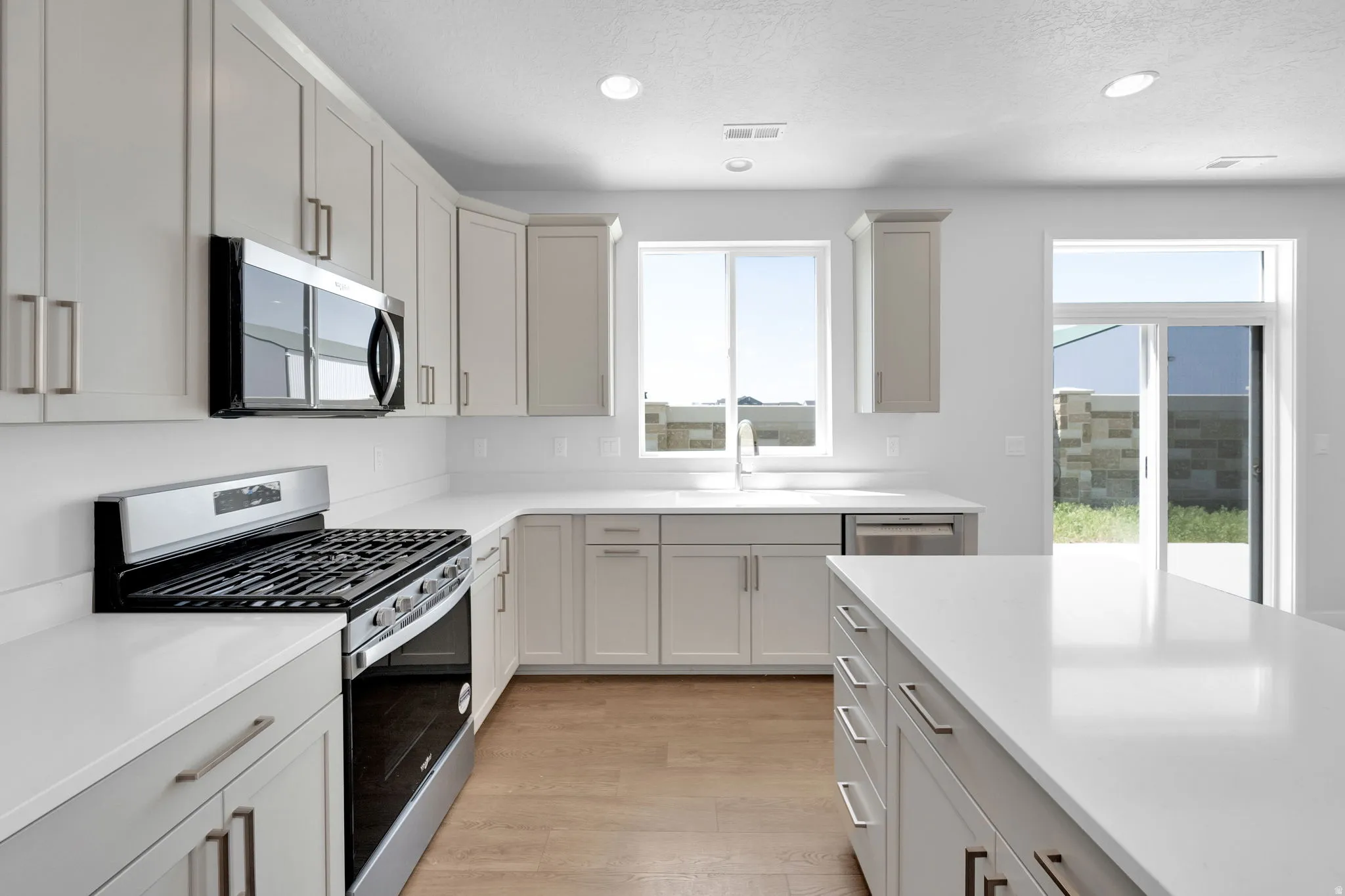 Modern kitchen featuring light gray cabinetry with brushed nickel hardware, white countertops, stainless steel appliances, and wood-finish flooring
