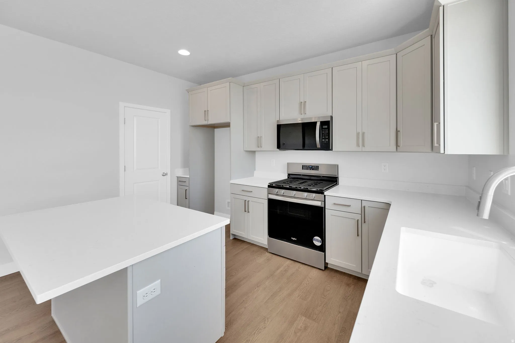 Contemporary kitchen featuring light wood-finish flooring, white countertops, light gray cabinetry, stainless steel appliances, and a central island with integrated outlets
