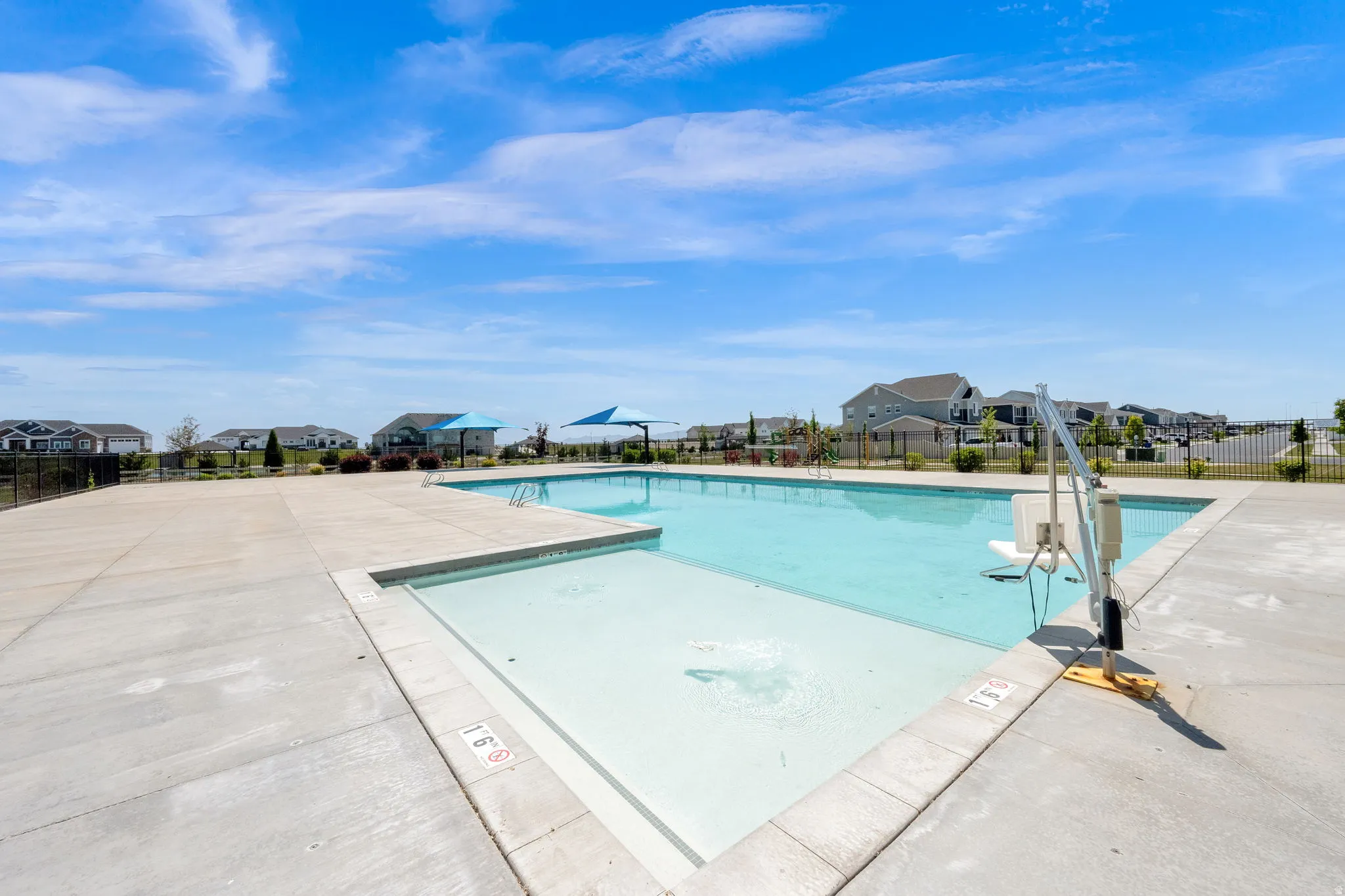 Community swimming pool with a concrete deck, integrated shallow water area, and a pool lift