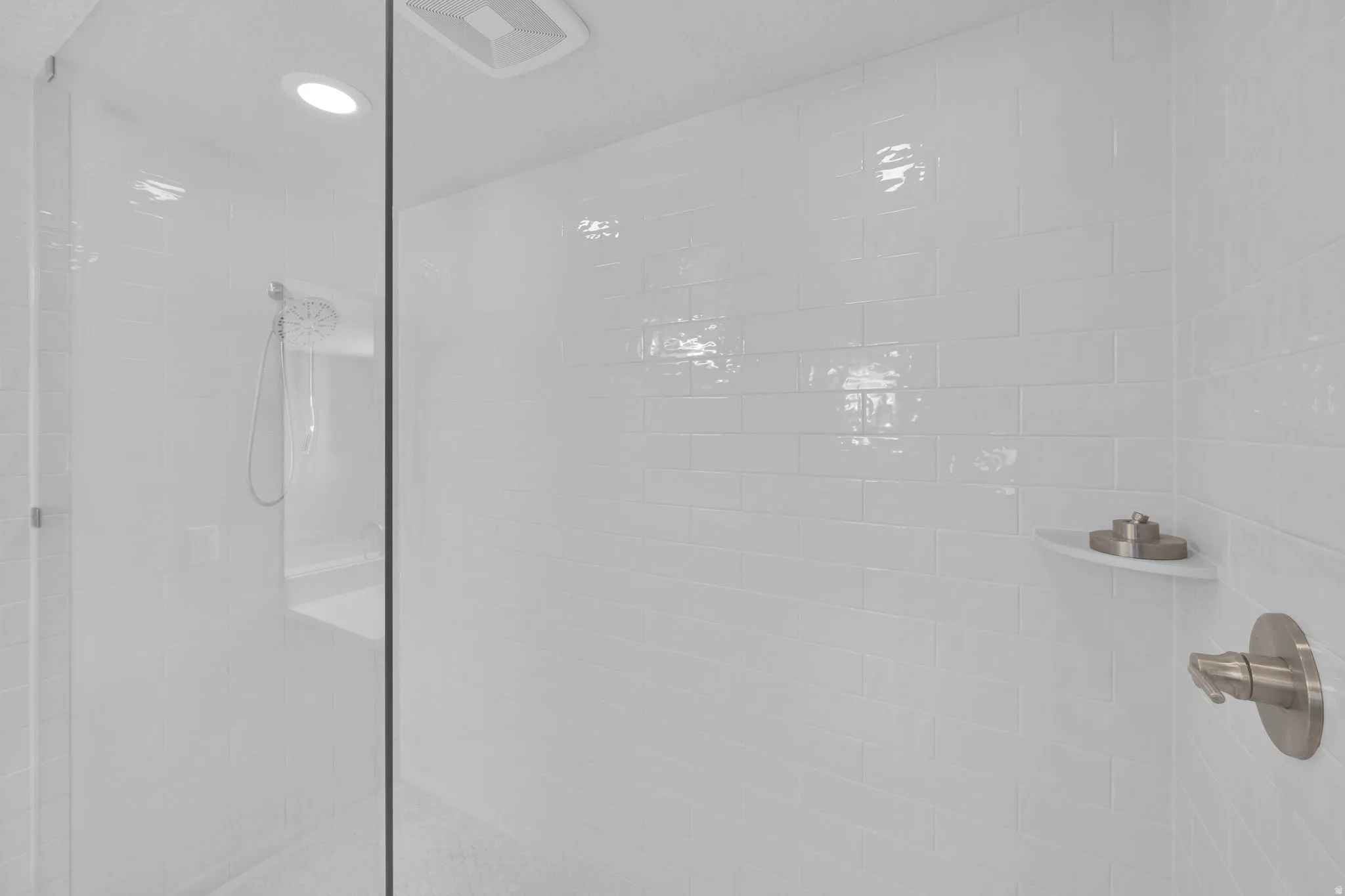 Walk-in shower featuring white subway tile, brushed nickel fixtures, a built-in corner shelf, and a glass enclosure