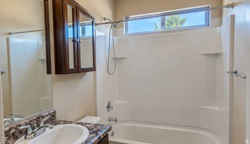 White bath and shower combination with chrome fixtures, a horizontal window, and integrated shelving