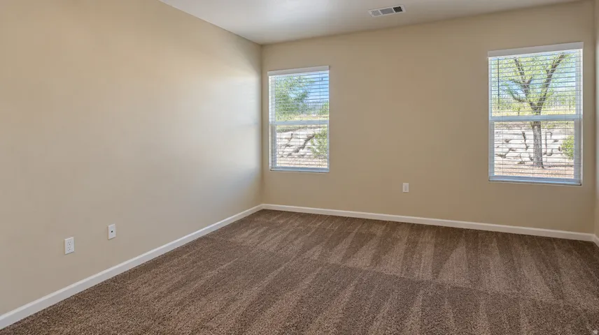 Neutral tone painted walls, textured carpet flooring, and two windows with horizontal blinds