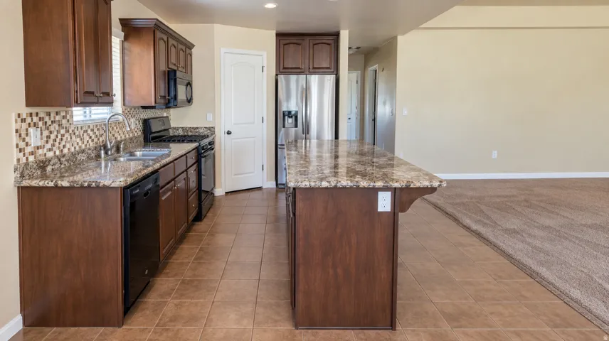 Kitchen featuring wood-finish cabinetry, stone-look countertops, stainless steel appliances, a tiled backsplash, and an island with bar seating