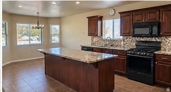 Kitchen featuring dark wood-finish cabinetry, black appliances, a stone backsplash, a large center island with a stone countertop, and recessed lighting