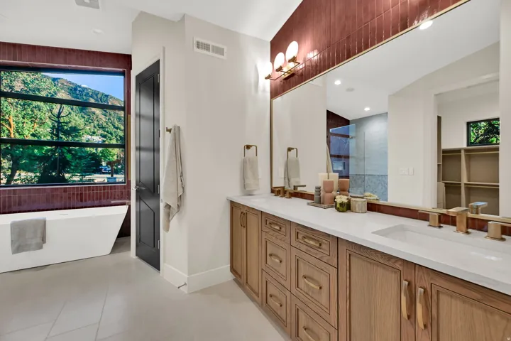 Spacious bathroom featuring a freestanding tub, large picture window, dual vanity with undermount sinks, wood-finish cabinetry, and a full-width mirror