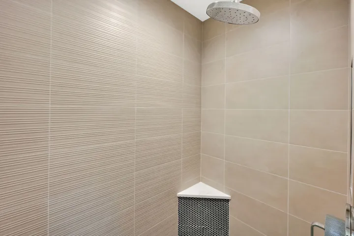 Shower enclosure featuring a rain shower head, textured wall tiling, smooth wall tiling, and a corner shelf with mosaic tile accents