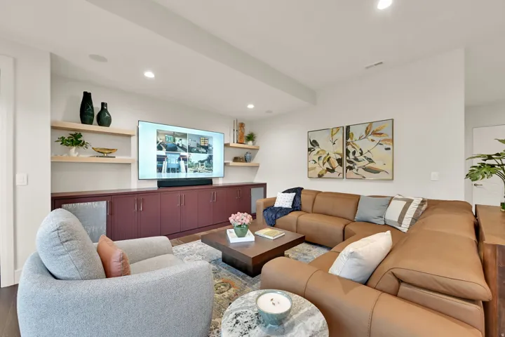 Recessed lighting illuminates a spacious living area featuring built-in cabinetry with a deep red finish, light wood floating shelves, and wood-finish flooring