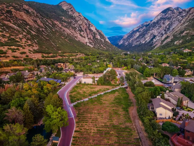 Mountainous terrain framing a verdant valley, featuring a residential area with mature trees and a curving roadway