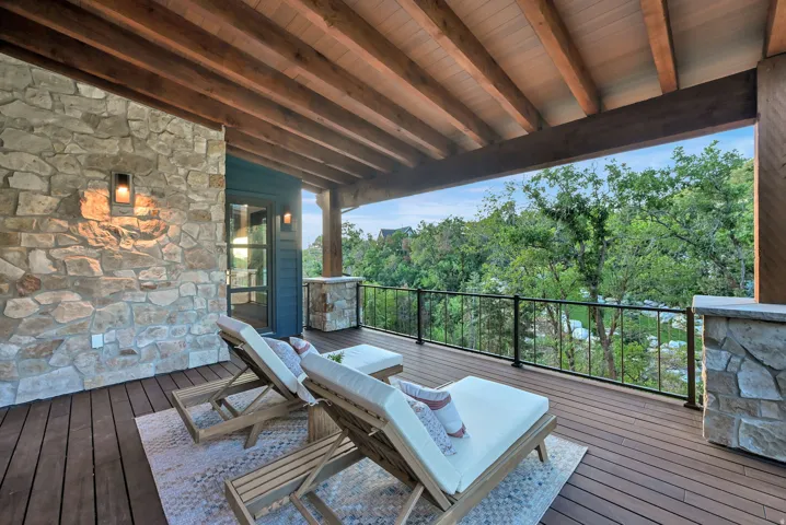 Spacious covered deck featuring a natural wood-finish ceiling with exposed beams, composite decking, and a stone accent wall