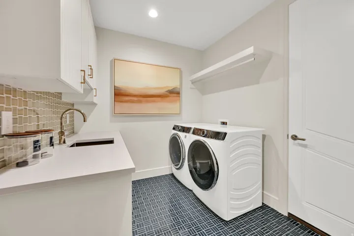 Utility room featuring a built-in sink with a gooseneck faucet, white cabinetry with gold-tone hardware, and a mosaic tile backsplash