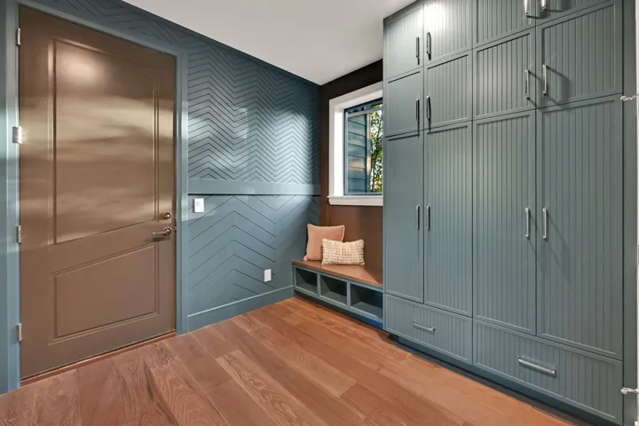 Entryway featuring a Dutch door, chevron-patterned accent wall, built-in window bench with storage, floor-to-ceiling cabinetry with beadboard detailing, and wood-finish flooring