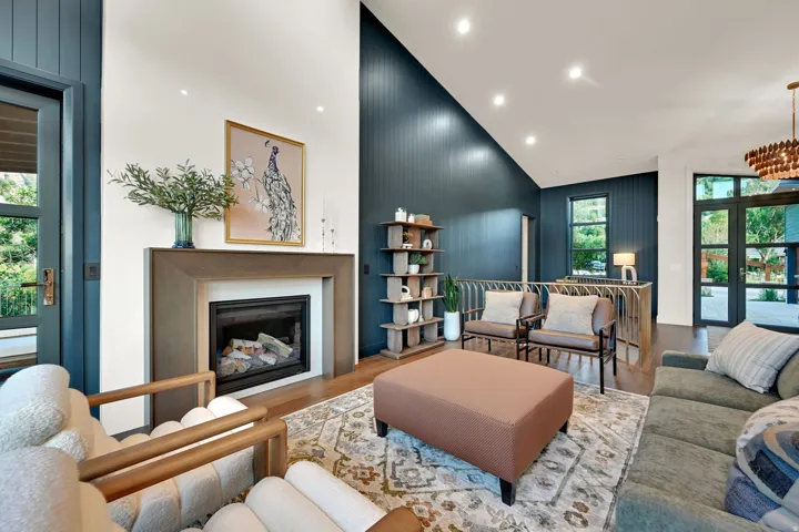 Living area featuring a gas fireplace with a wood mantle, rich wood-finish flooring, and a soaring vaulted ceiling