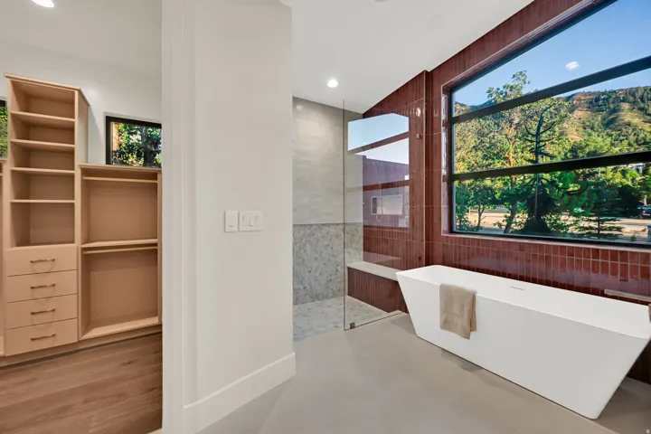 Freestanding soaking tub with a substantial window, large walk-in shower with a glass enclosure, and built-in closet system with drawers and shelving