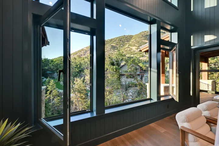Expansive picture windows with operable sections frame a mountainous, tree-lined landscape