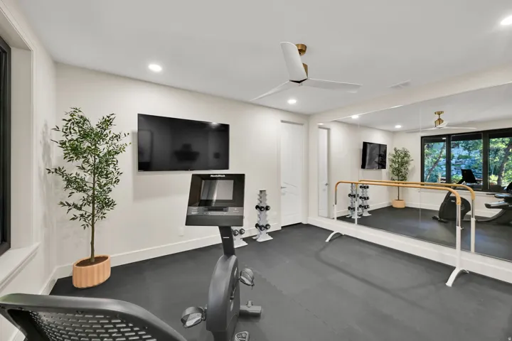 Dedicated fitness space featuring rubberized flooring, a full-wall mirror, and a ballet barre