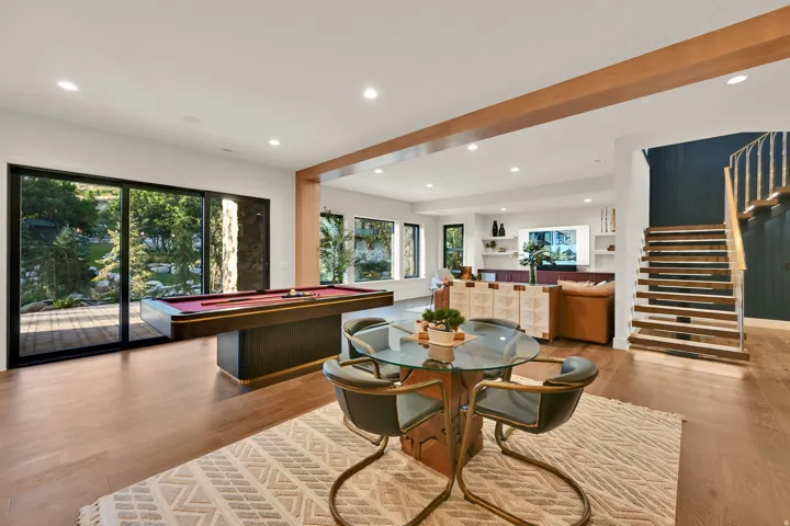 Spacious recreation room featuring large sliding glass doors, recessed lighting, wood-finish flooring, an exposed beam, and an open staircase with metal railings