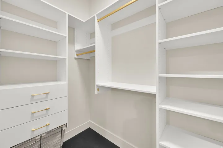 Custom closet system featuring white shelving and drawers with gold-tone hardware