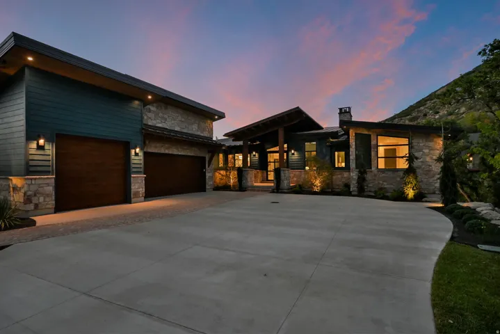 Stone and wood-finish siding exterior featuring multiple rooflines, a wide concrete driveway, and integrated outdoor lighting