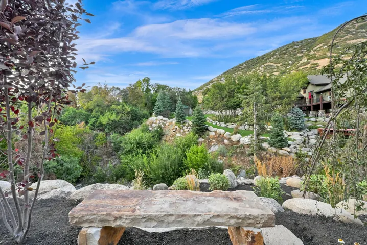 Expansive natural landscaping featuring a rustic stone bench, diverse mature trees, and a mountain backdrop