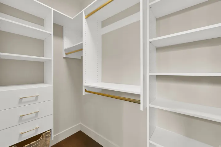 Built-in closet system featuring white shelving, integrated drawers with gold-tone hardware, and multiple hanging rods