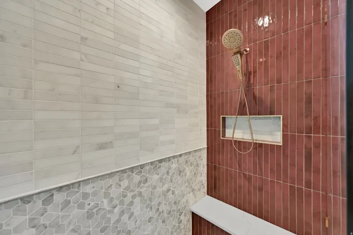 Shower enclosure featuring a built-in bench, recessed niche, and a combination of red vertical subway tiles, grey geometric mosaic tiles, and white horizontal subway tiles